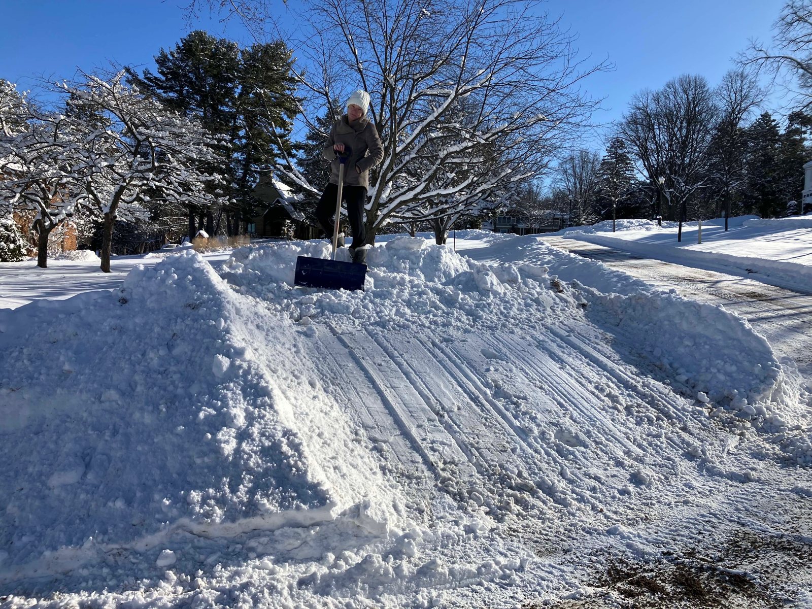 A resident with a shovel beside a plow pile taller than she is